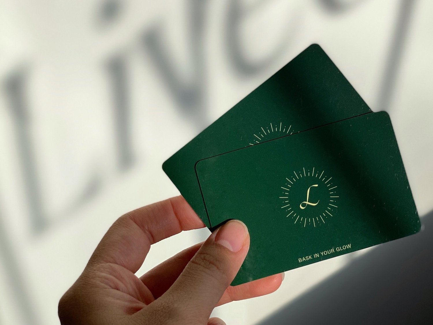 A hand holding Liveo Beauty's forest-green gift cards with a gold sunburst monogram